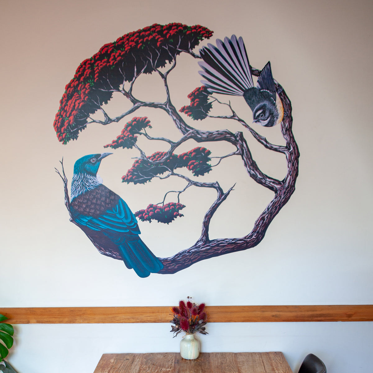 Circular tūī and native botanical wall art above a table