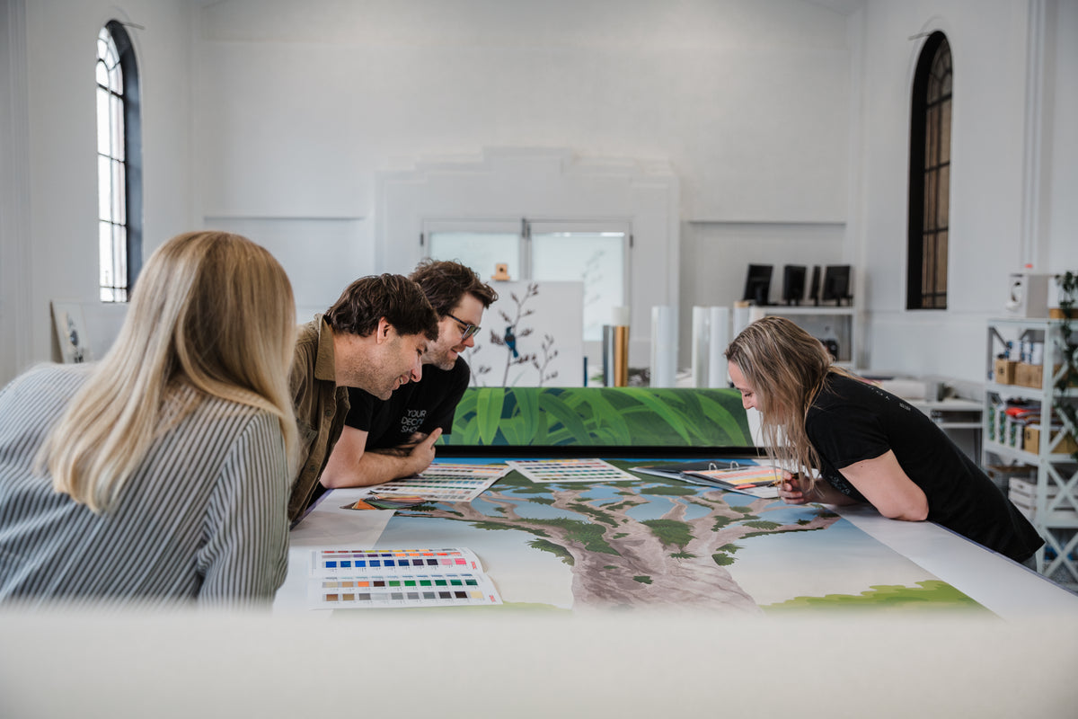 Jess, Kieran, Antony and Shayla reviewing illustrated mural artwork around a table in the YDS Studio workshop