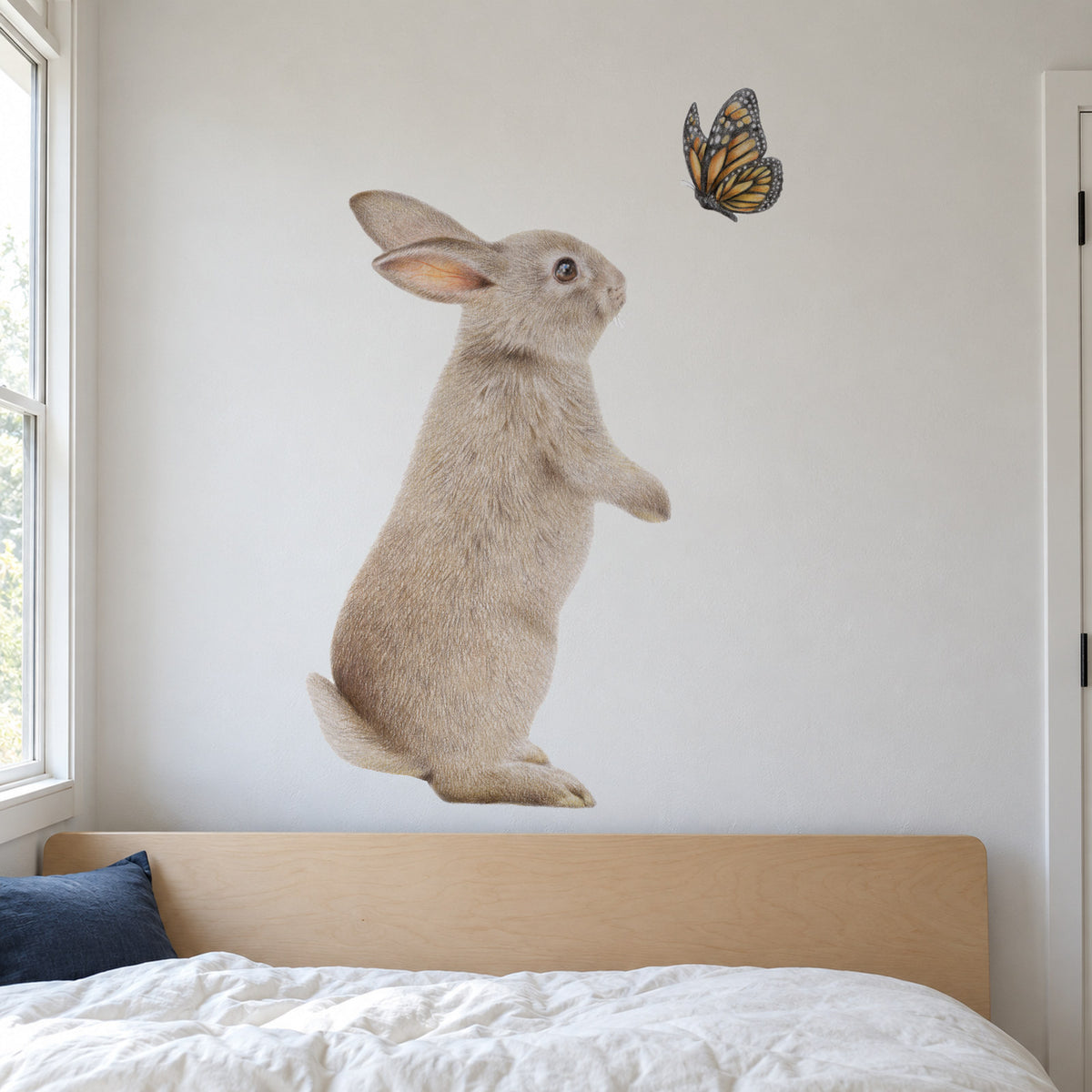 Bunny and Butterfly by Olivia Bezett, wall decal room mock-up in a bedroom above a blue bed.