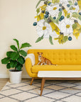 Yellow sofa with a dog sitting on it, large floral mural on the wall, and a plant in the corner.