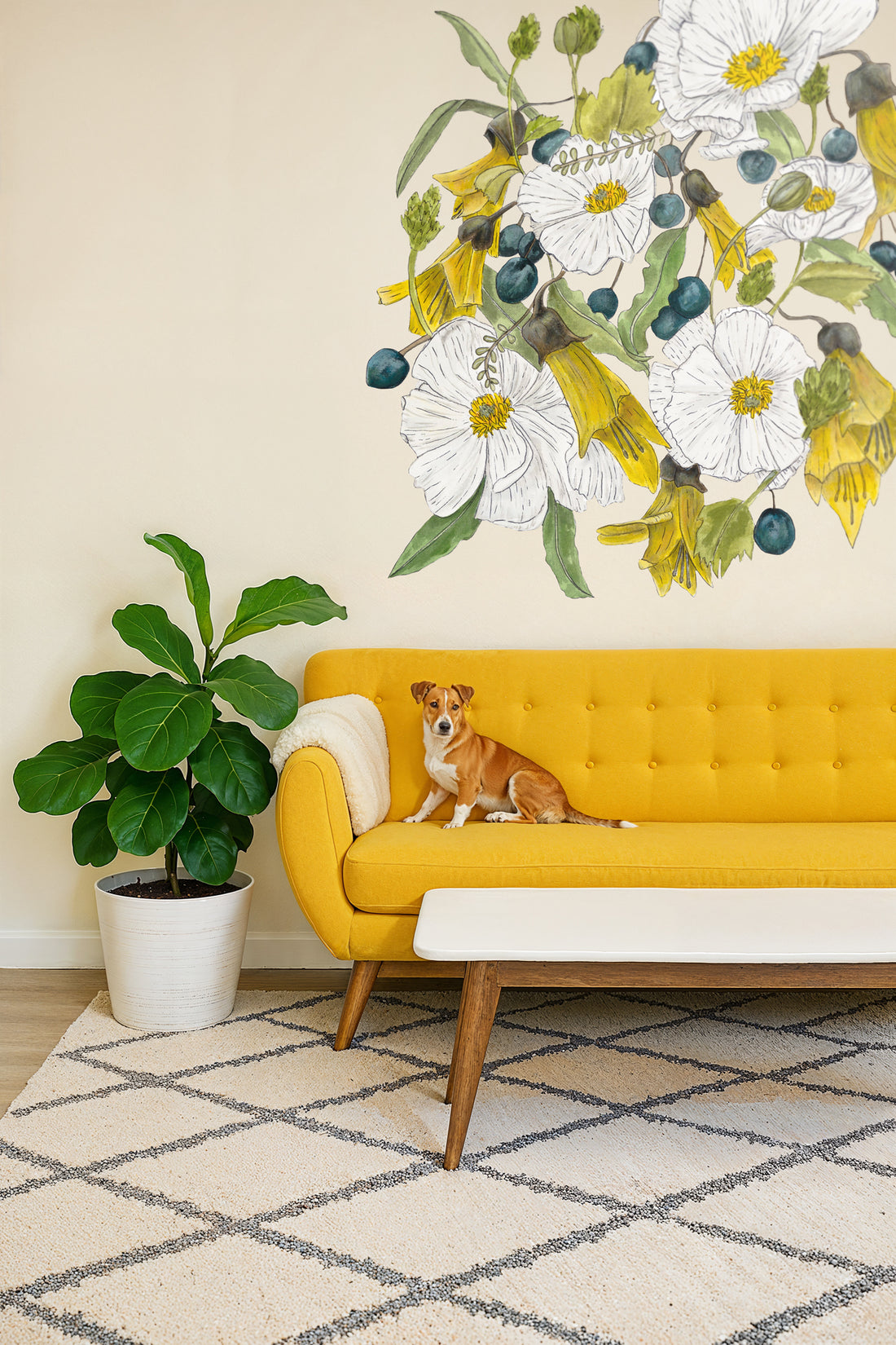 Yellow sofa with a dog sitting on it, large floral mural on the wall, and a plant in the corner.