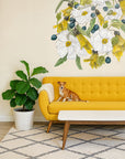 Yellow sofa with a dog sitting on it, large floral mural on the wall, and a plant in the corner.